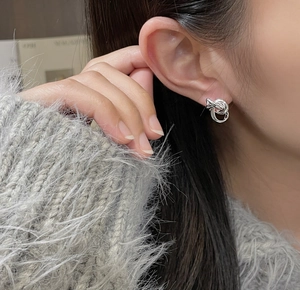 Macro shot of minimalist silver twisted knot stud earring on a female model's ear
