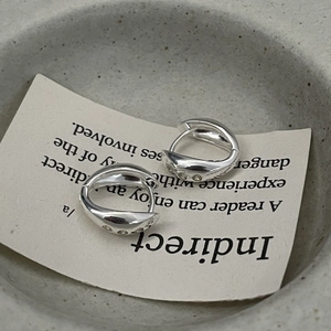 Detail view of silver streamlined earrings with three inset zircons on textured backdrop