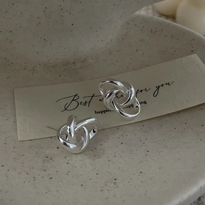 Detail view of S925 sterling silver knotted stud earrings on a textured ceramic dish