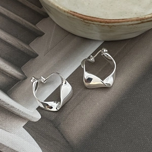 Detailed view of polished irregular twisted silver earrings on minimalist grey background