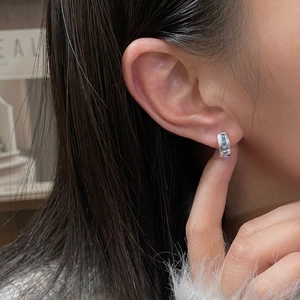 Close-up of a silver ear cuff featuring square blue zircon stones worn on the ear