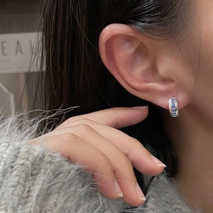 Close-up of elegant silver hoop earrings with blue zircon stones on a female model