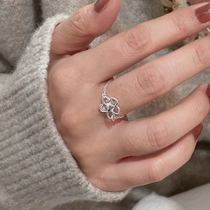 Detail of adjustable S925 silver hollow flower chain ring worn on finger with a cozy background