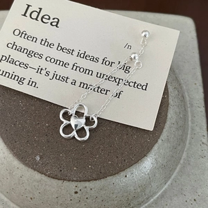 Macro shot of silver flower chain earrings with heart detail on a textured ceramic base