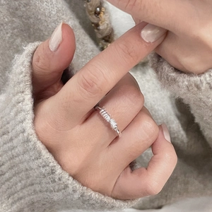 Gros plan d'une bague nouée en argent S925 sur un doigt avec un fond de pull en laine gris chiné