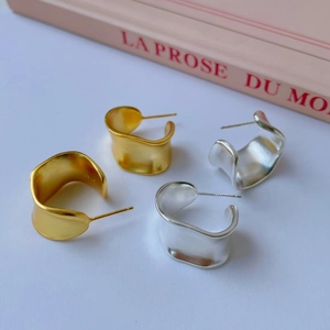 Macro detail of matte S925 sterling silver curved wave stud earrings in gold and silver