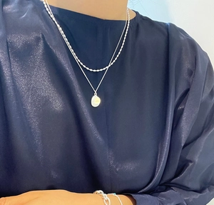 Detail of layered S925 sterling silver beaded necklace with oval youth pendant on model