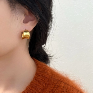 Close-up of wide matte gold curved earring worn by a model in an orange sweater