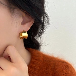 Close-up of elegant gold thick C-shaped hoop earrings on a model with warm knitwear