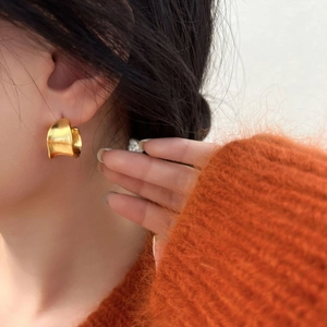 Close-up of a minimalist curved gold earring with polished finish worn on a real model
