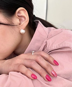 Close-up of elegant white pearl stud earrings and a silver knot ring worn by a model