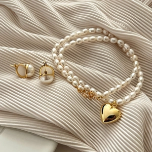 Close-up of double-layer pearl necklace with gold heart pendant and matching pearl earrings