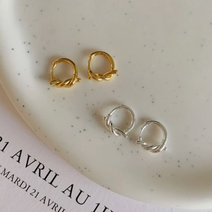 Détail des boucles d'oreilles nœud dorées et argentées sur un plateau avec un magazine