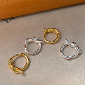 Gros plan de boucles d'oreilles nouées dorées et argentées sur un fond texturé chaud