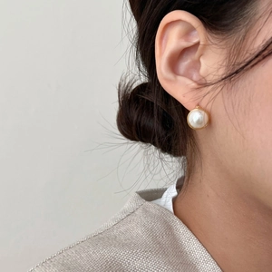 Close-up of minimalist gold-plated pearl hoop earrings worn by a model in soft light