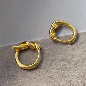 Vue détaillée de boucles d'oreilles nœud dorées polies avec finition miroir sur fond texturé