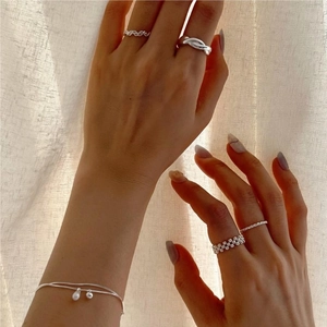 Dettaglio di anelli minimalisti in argento e bracciale di perle sulla mano di una modella