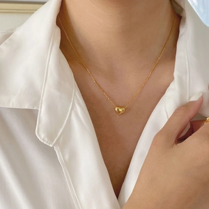 Gros plan d'un délicat collier avec pendentif cœur doré porté par une femme en chemisier