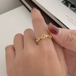Detail shot of a hollow heart chain ring in gold finish worn on a finger