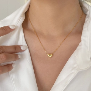 Gros plan d'un pendentif cœur 3D minimaliste en finition dorée sur une chaîne délicate