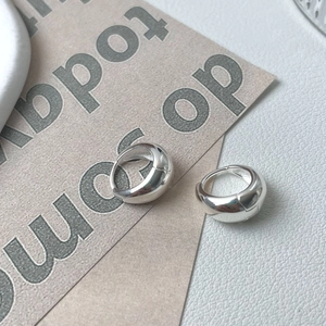 Macro shot of polished thick silver hoop earrings on a textured white leather background