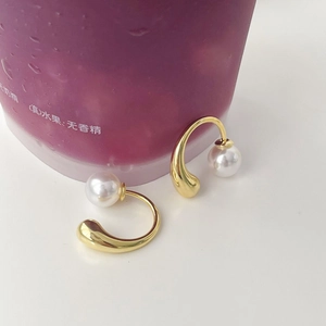 Macro view of gold U-shaped drop earrings featuring round white pearls in a minimalist design