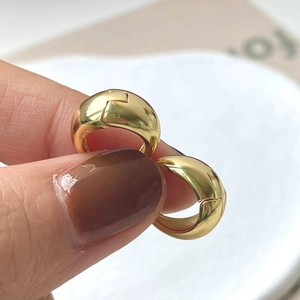 Close-up of chunky gold hoop earrings with mirror-polished finish and hinge closure
