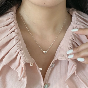 Détail d'un collier avec pendentif coeur en argent S925 porté au cou par une femme