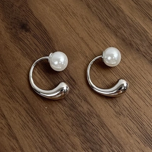 Macro shot of silver C-shape drop earrings with pearls on dark walnut wood surface
