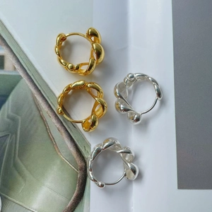 Détail de boucles d'oreilles créoles torsadées en finitions or et argent polies