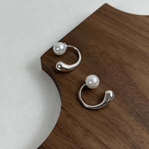 Detailed view of teardrop silver earrings and white pearls on dark wood texture background