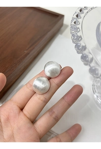 Detailed view of large silver brushed matte ball stud earrings held by hand