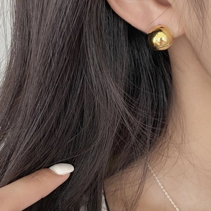 Macro shot of gold spherical stud earring with high polished finish on a person