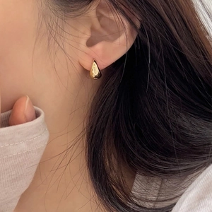 Detailed view of polished gold teardrop earrings worn by a model in a minimal style