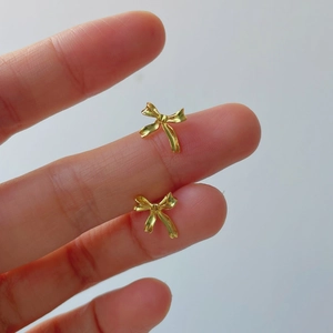 Gros plan détaillé des boucles d'oreilles nœud doré montrant la taille réelle en main