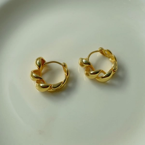 Vue détaillée de boucles d'oreilles créoles torsadées dorées sur céramique
