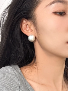 Detailed close-up of a large brushed silver ball stud earring on a model earlobe