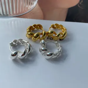 Gros plan de boucles d'oreilles créoles torsadées en argent et or sur présentoir