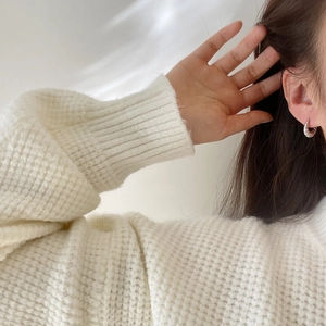 Close-up of silver croissant twisted hoop earring on model wearing white knit sweater