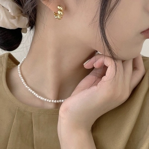 Gros plan sur une boucle d'oreille torsadée dorée et un collier de perles fines