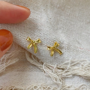 Gros plan de boucles d'oreilles nœuds dorés avec texture sur fond de tissu beige