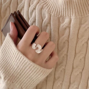 Close-up of minimalist irregular wave silver ring worn on index finger with cozy sweater