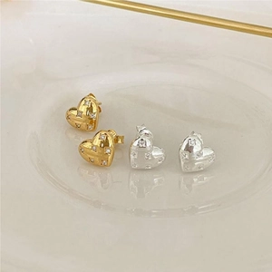 Close-up of gold and silver heart stud earrings with cubic zirconia on a ceramic tray