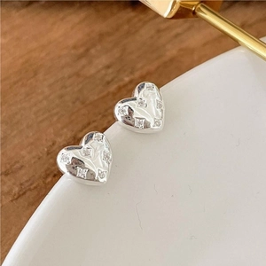 Macro shot of silver heart studs featuring five micro-set zircons on a white ceramic stand