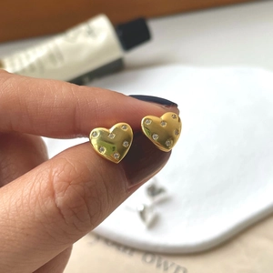 Close-up of golden heart earrings with sparkling cubic zirconia on a hand