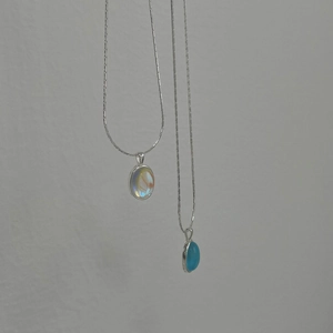 Detail of silver snake chain necklaces with oval iridescent opal and blue gemstones