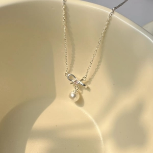 Detailed shot of S925 silver bow necklace with pink crystal and white pearl on beige ceramic