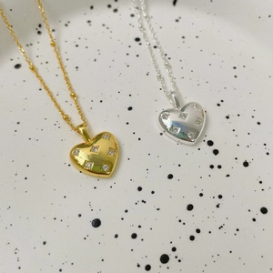 Macro detail of gold and silver heart pendants with cubic zirconia on a ceramic plate