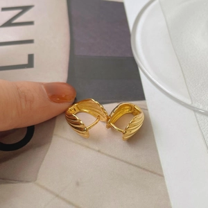 Detail of gold shell-style earrings with wavy texture and secure clasp closure