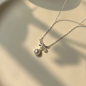Macro view showing silver bow pendant with pink stone and white pearl bead on necklace